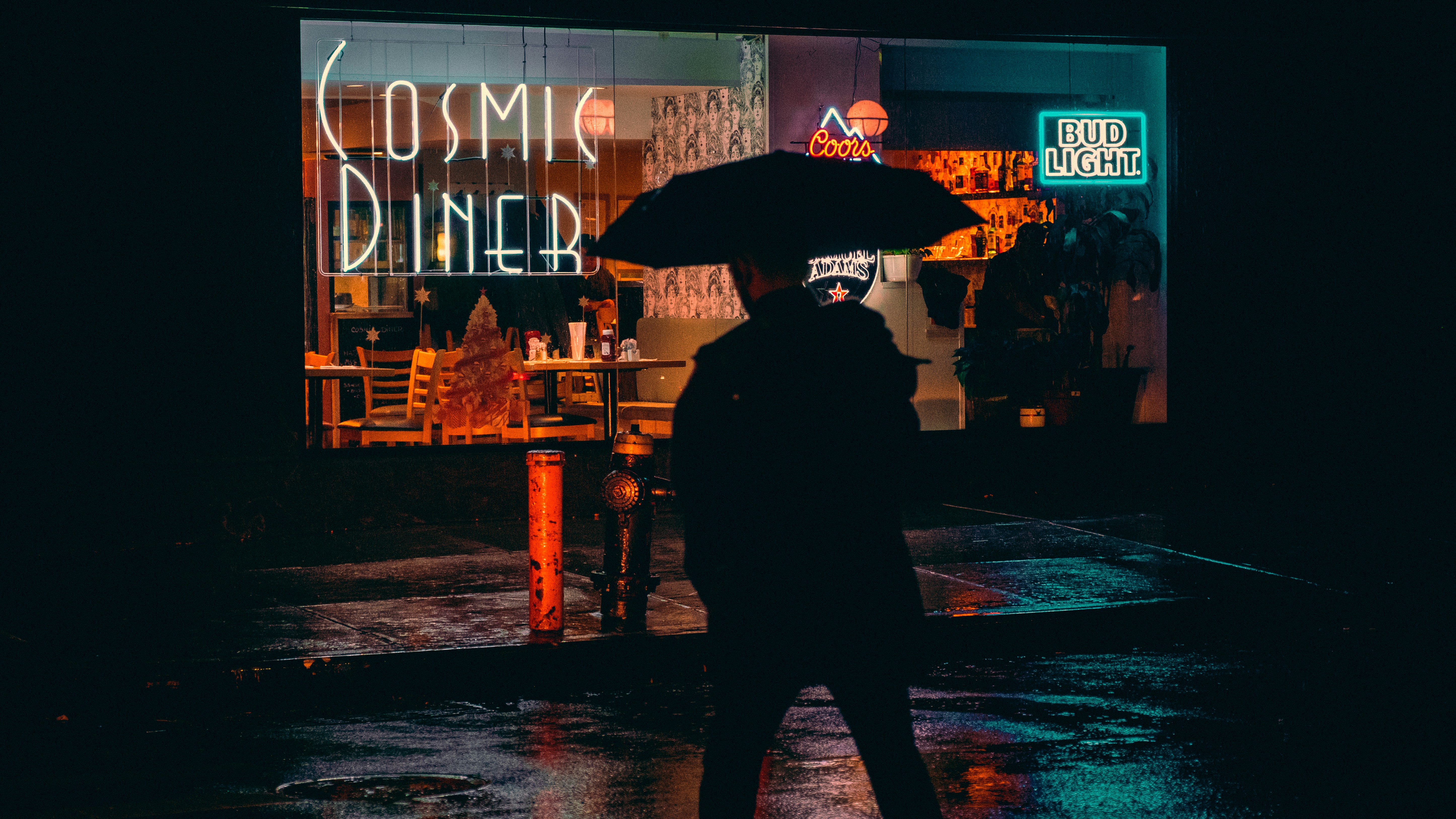 Cosmic Diner at night in Manhattan. A man with an umbrella is walking towards the restaurant. Photo by Luiz Guimaraes.