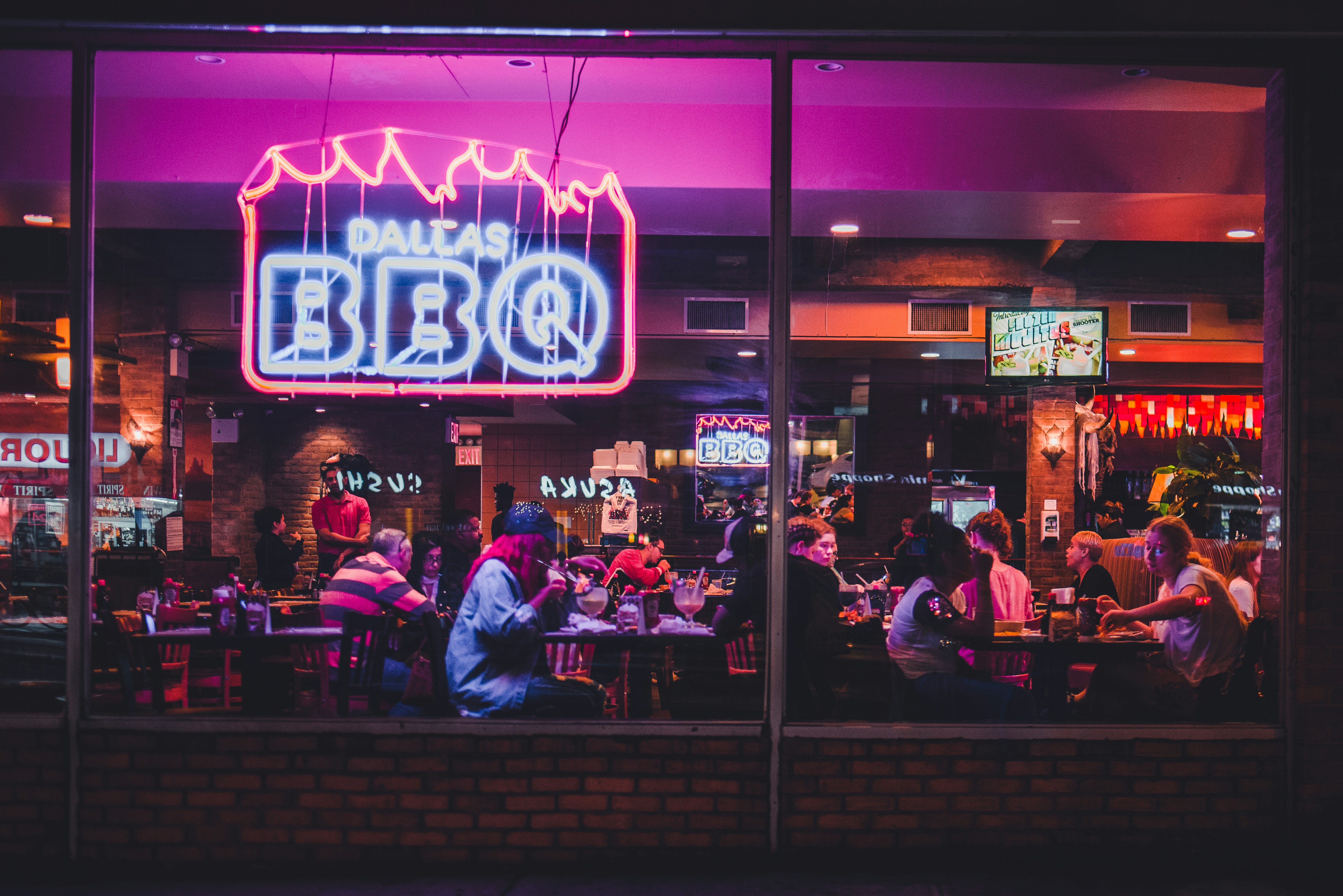 Dallas BBQ at night in Chelsea, Manhattan. Diners are seen inside eating and drinking. Photo by Nathalia Segato.