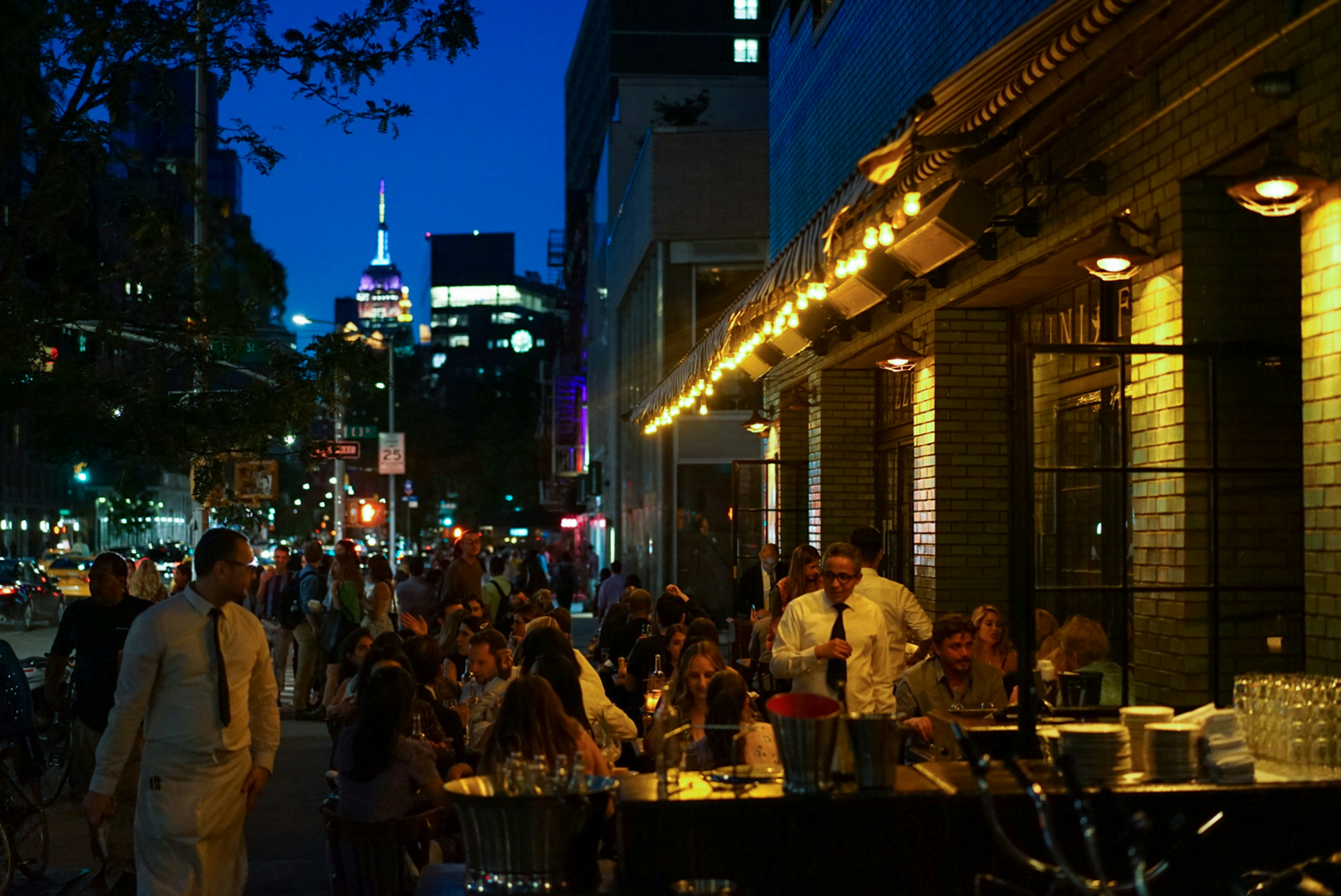 Nighttime sidewalk dining in Manhattan, with a view of the Empire State Building in the background. Photo by Megan Bucknall.